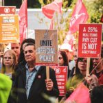 Group of people in London protesting against wage cuts, holding signs demanding fair pay.