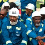Construction workers in blue uniforms and white helmets during a break outdoors.