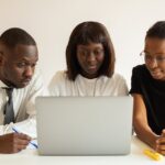 Three professionals working together on a project using a laptop in an office setting.